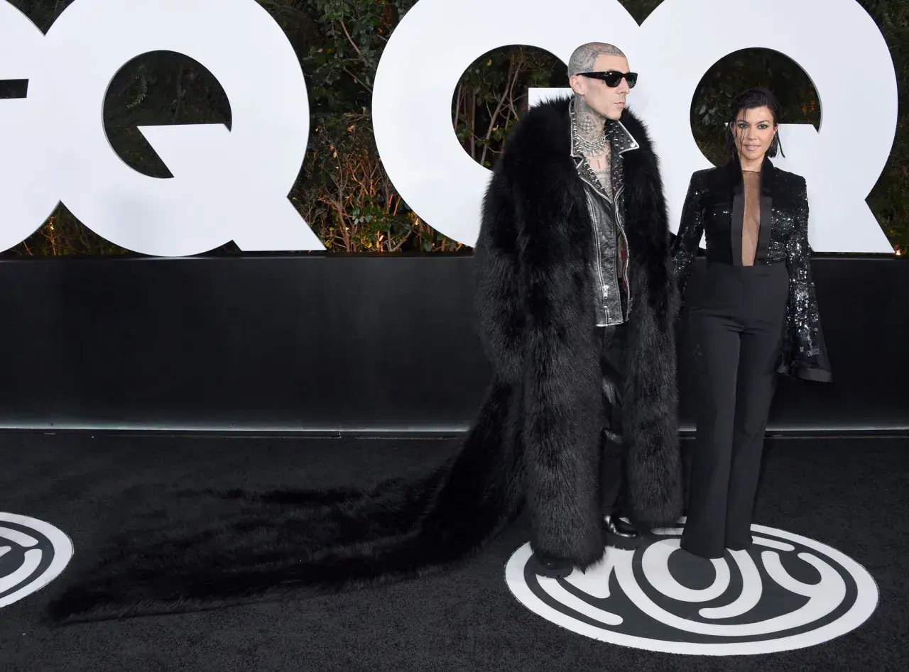 Travis Barker i jego żona Kourtney Kardashian na ściance GQ. Travis w ekstrawaganckim futrze, Kourtney w eleganckim garniturze.
