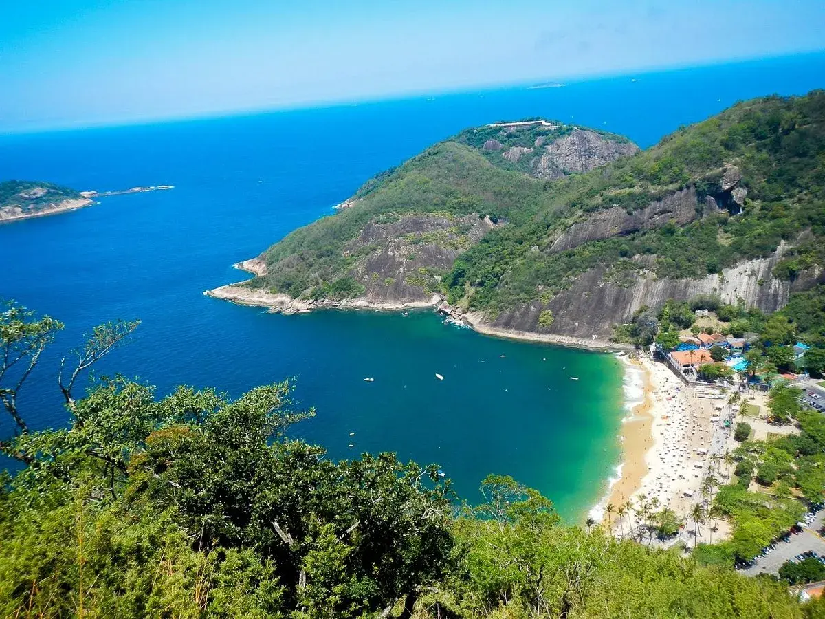 Blick vom Morro da Urca auf eine Bucht mit Strand, Palmen und dem tiefblauen Meer.