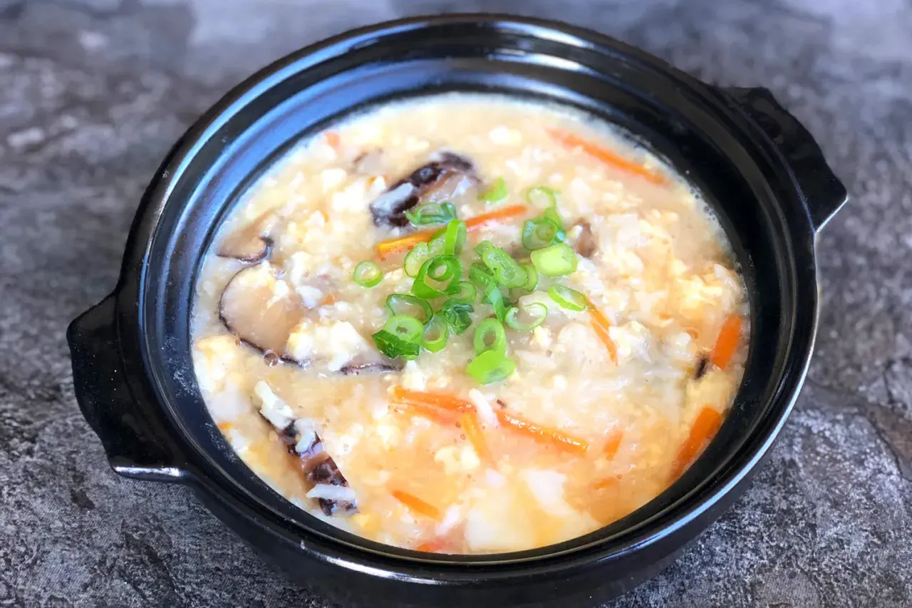 A comforting bowl of Japanese rice soup, also known as okayu, filled with tender rice, shiitake mushrooms, shredded carrots, and scrambled egg, garnished with fresh green onions.