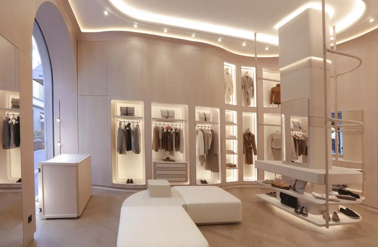 Interni negozio di abbigliamento con abiti eleganti appesi, borse e scarpe in esposizione. L'ambiente è moderno e luminoso, con un design minimalista e finiture in legno chiaro.