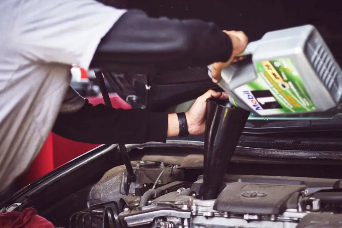 Un meccanico versa olio motore Mobil 1, con specifica API SN, nel vano motore di un'auto.