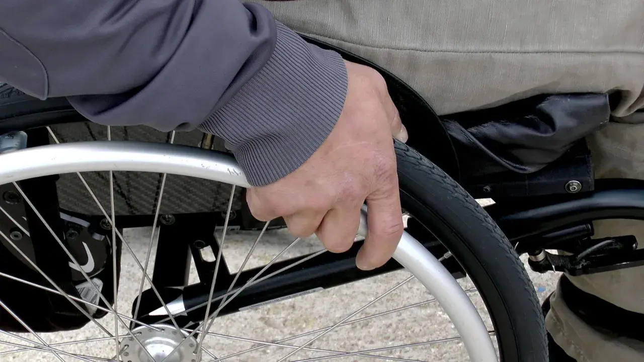 Mano che afferra la ruota di una sedia a rotelle per anziani, un ausilio essenziale fornito dall'ASL per garantire mobilità e autonomia.