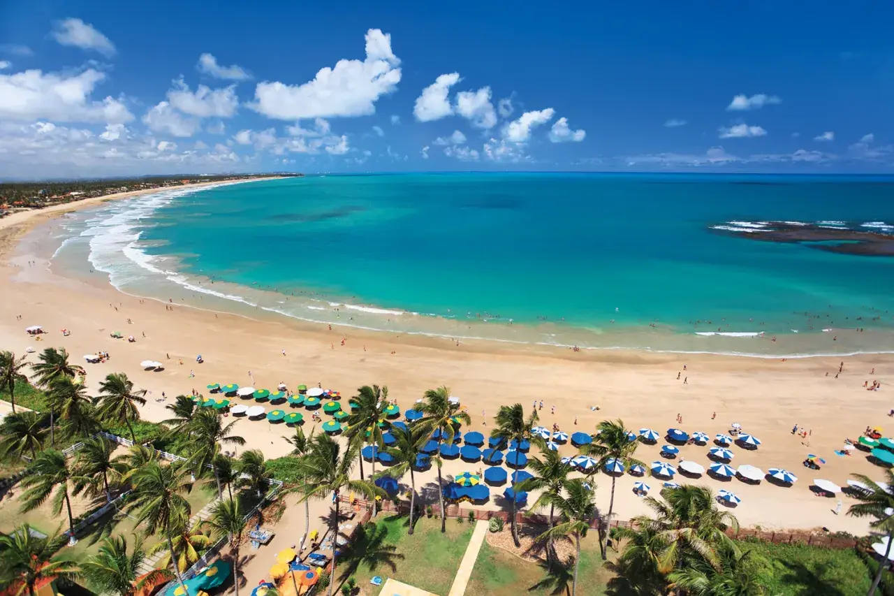 Traumhafter Strand von Porto de Galinhas mit türkisfarbenem Wasser, Palmen und vielen bunten Sonnenschirmen.