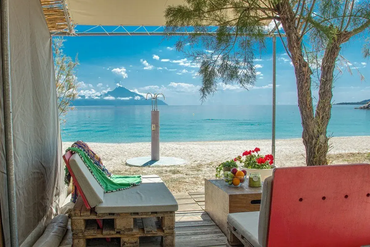 Relaks przy plaży w Armenistis Camping. Leżaki, stolik z owocami i widok na morze z górą w oddali.