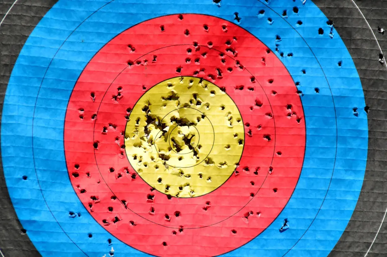 Tarcza strzelecka z licznymi dziurami po strzałach. Wiele trafień w środek, co świadczy o dobrym treningu do uzyskania pozwolenia na broń sportową.