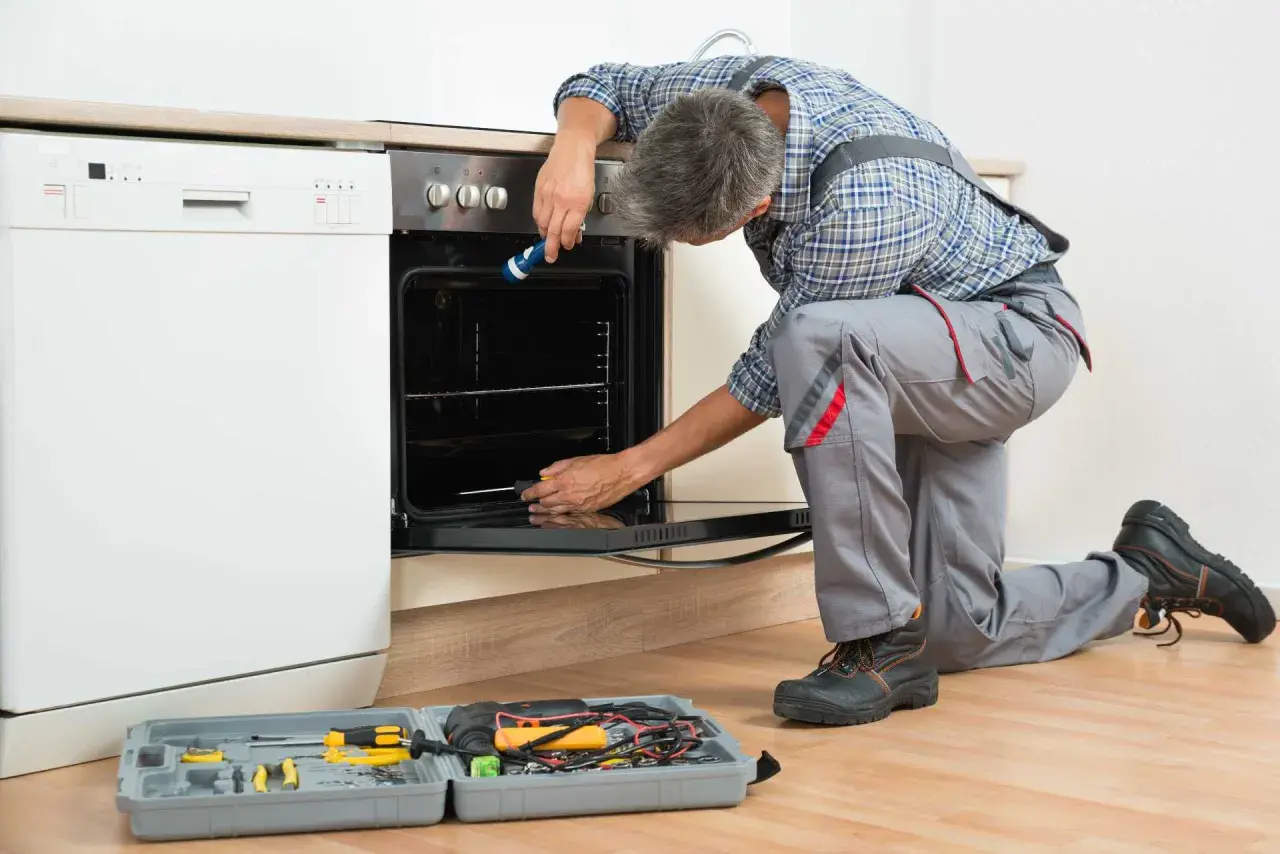Un technicien effectue le branchement d'un four encastrable, outils à portée de main.
