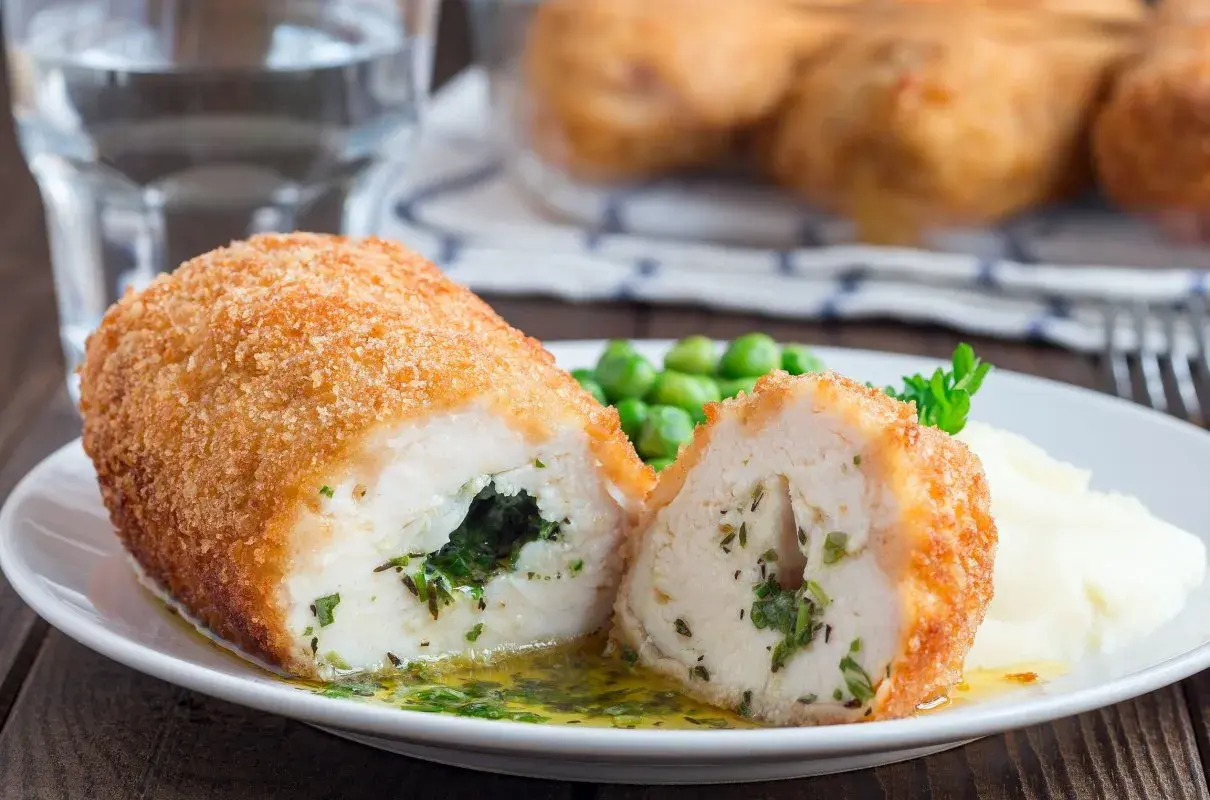Pyszny kotlet po kijowsku, chrupiący z zewnątrz, soczysty w środku, z zielonym nadzieniem. Podany z puree i groszkiem.
