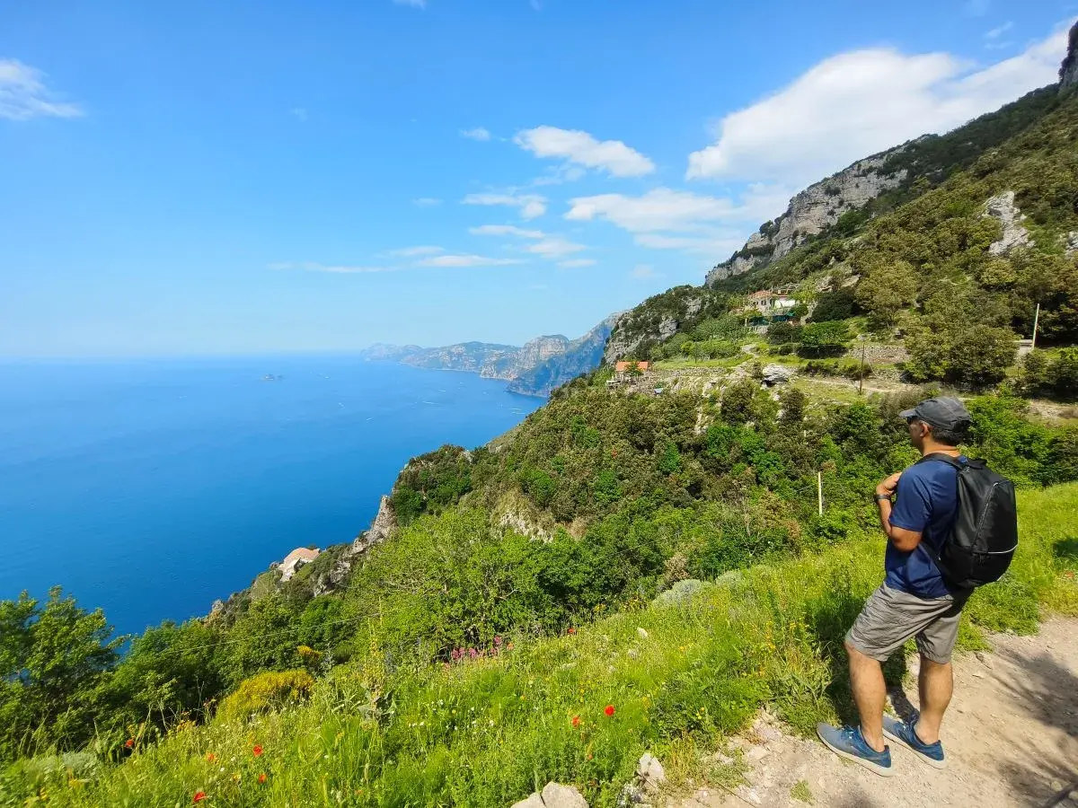 Hiker on a cliff path overlooking the blue sea and coastline.