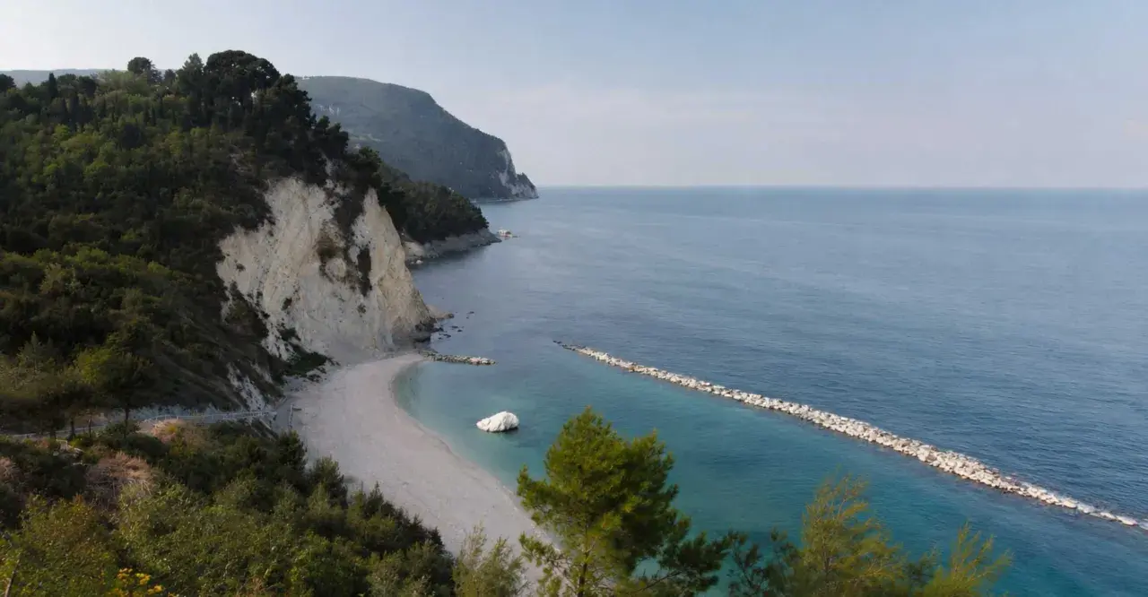 Scogliera verdeggiante e spiaggia bianca a Numana, con il lungomare che si estende verso il mare azzurro.