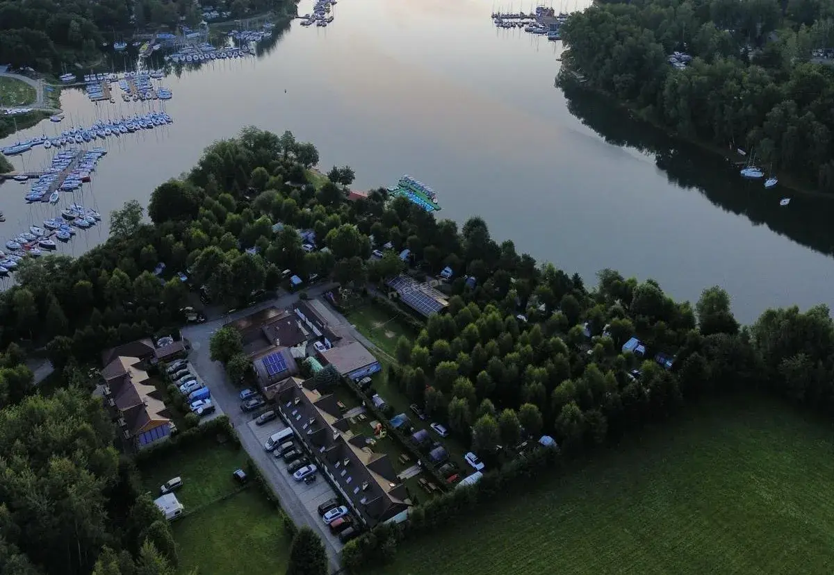 Malowniczy widok na camping w Polańczyku nad jeziorem, z łodziami na wodzie i zielonymi drzewami.