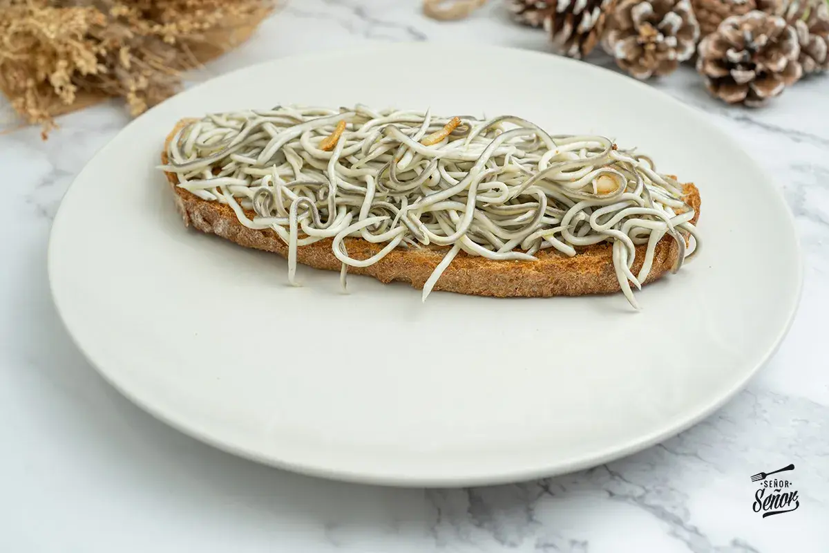 Tosta con gulas al ajillo, un clásico de las recetas con gulas, servida en plato blanco.
