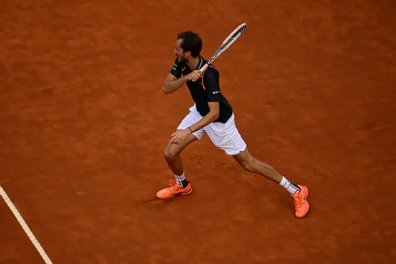 Tenisista wykonuje potężny **backhand** na ceglanej nawierzchni.