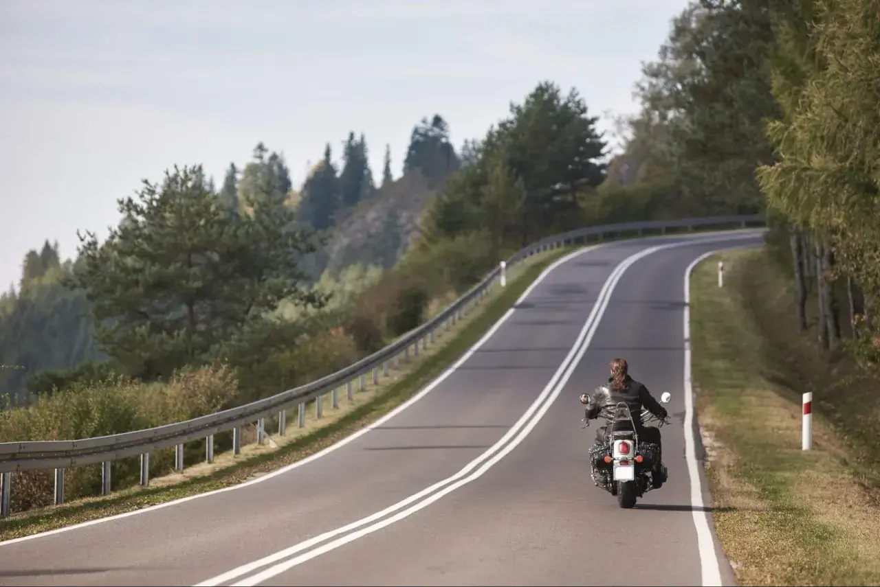 Motocyklista na zakręcie górskiej drogi, otoczony drzewami.