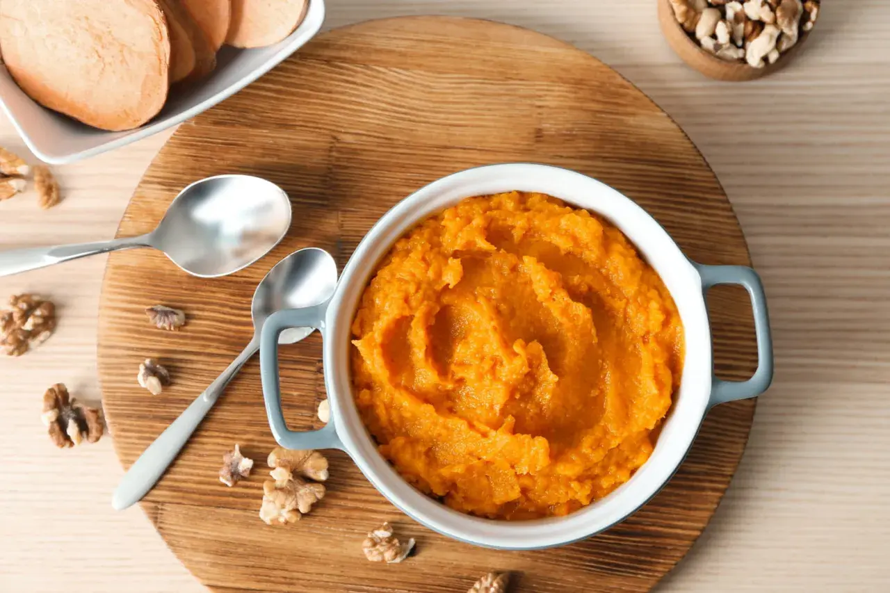 Un bol de purée de patate douce onctueuse, garni de noix et accompagné de tranches de patate douce.