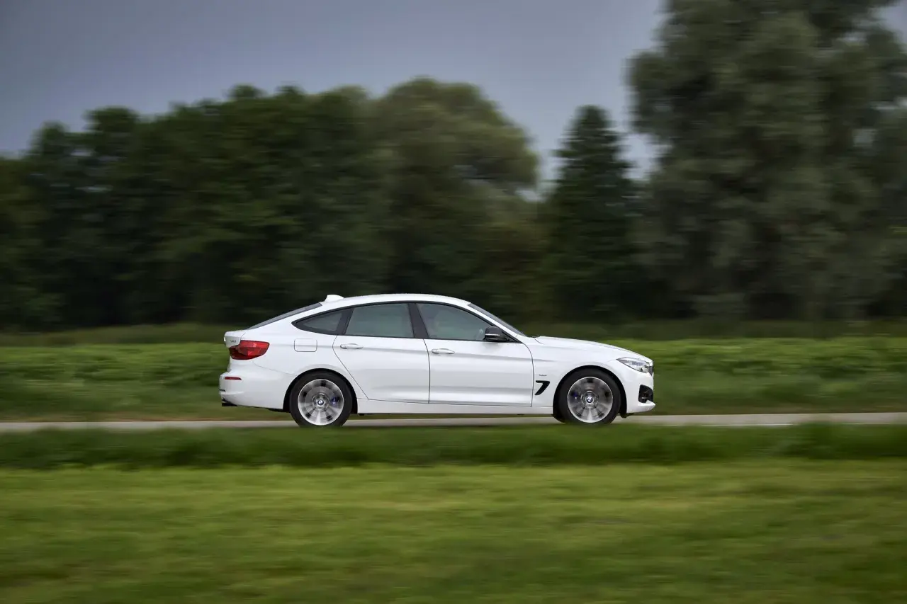 Białe BMW 330d mija zielone pola i drzewa, poruszając się z dużą prędkością.