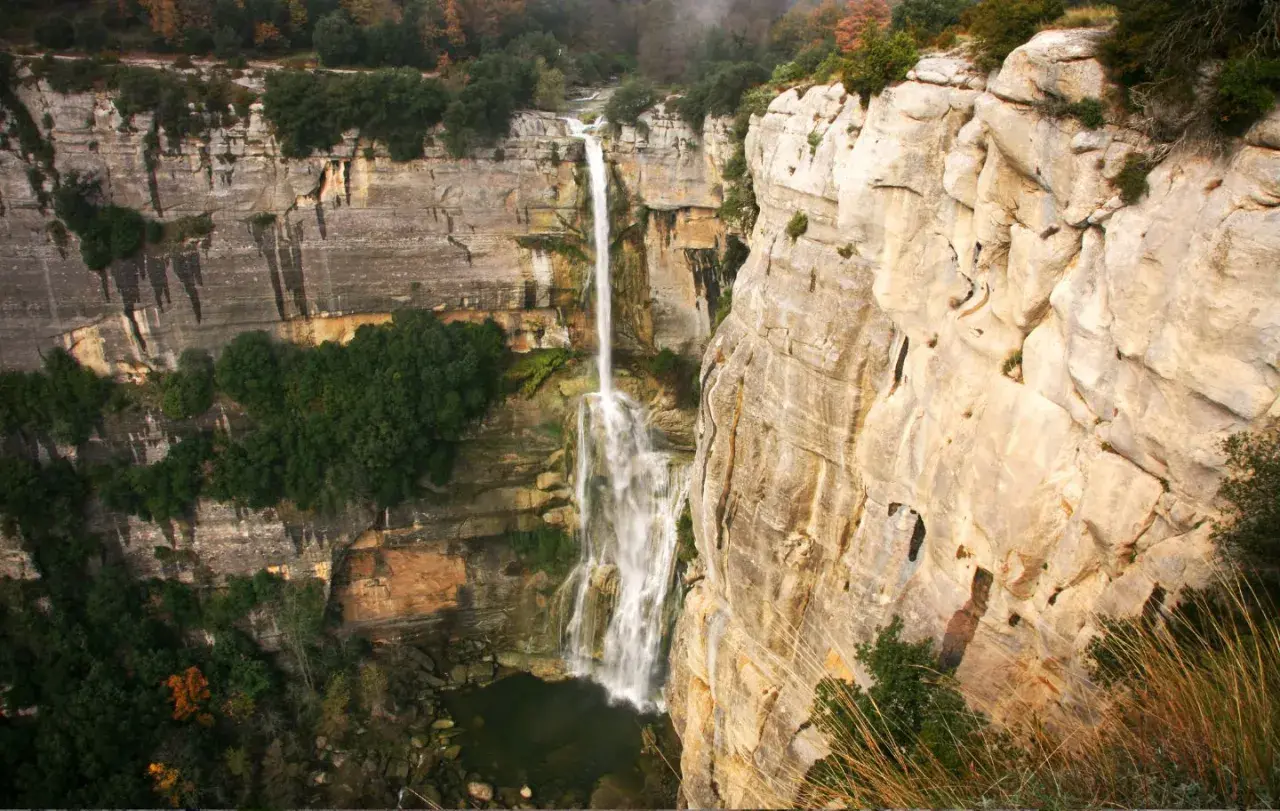 El imponente salt de Sallent cae desde lo alto de acantilados rocosos, rodeado de vegetación exuberante y un paisaje natural impresionante.