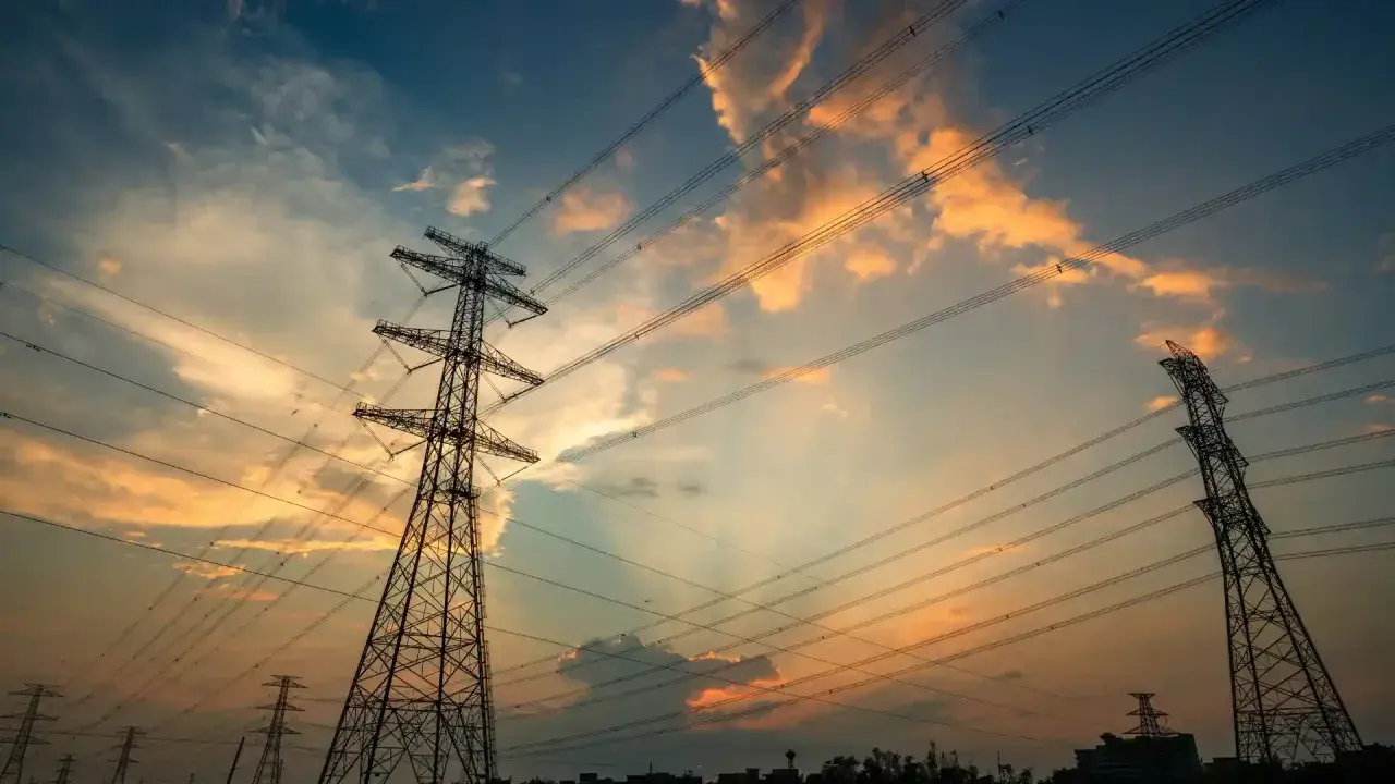Wieże energetyczne na tle zachodzącego słońca, z chmurami w odcieniach pomarańczy i błękitu. THD.