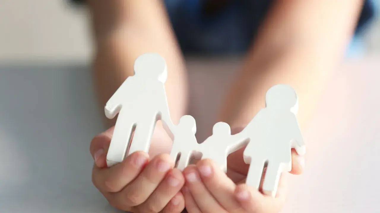 Hände halten weiße Holzfiguren einer Familie. Dies symbolisiert die Verantwortung für ein Kind und die finanzielle Unterstützung, die damit einhergeht.