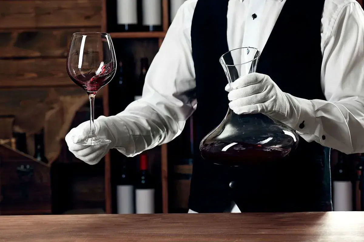 Kellner mit Handschuhen hält Weinglas und Karaffe. Eine Flasche Wein ergibt etwa 5 Gläser.