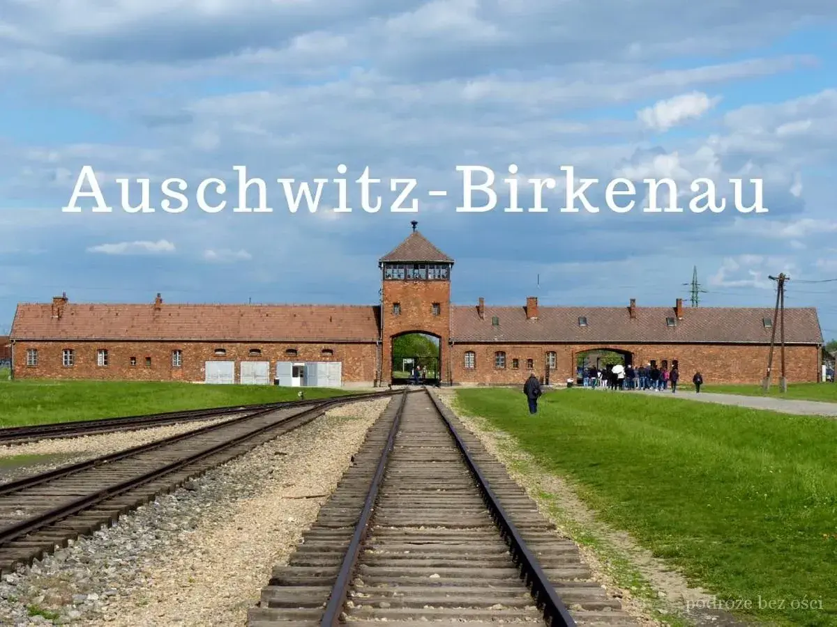 Brama obozu Auschwitz-Birkenau, gdzie jest to miejsce pamięci. Tłum zwiedzających podąża torami kolejowymi.