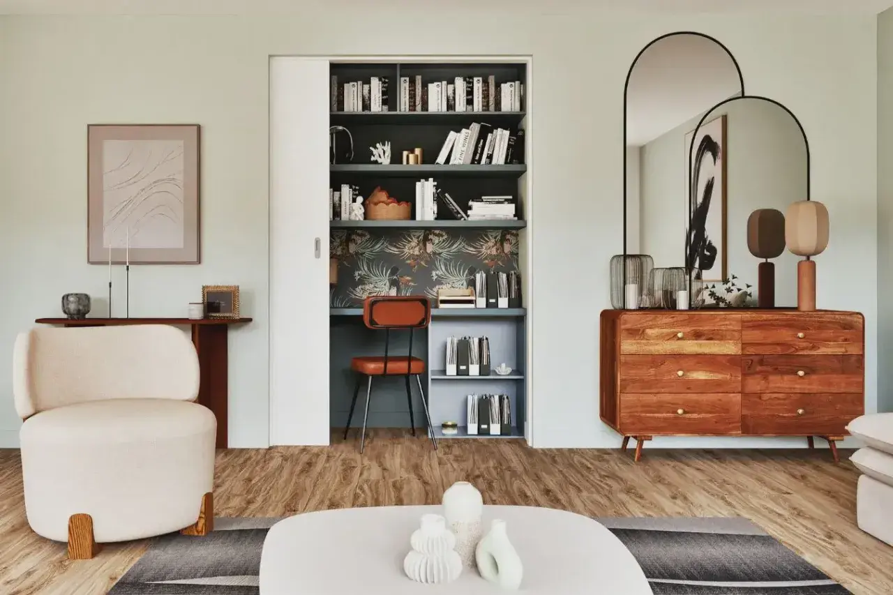 Un bureau placard aménagé avec une chaise orange, des étagères remplies de livres et un papier peint tropical.