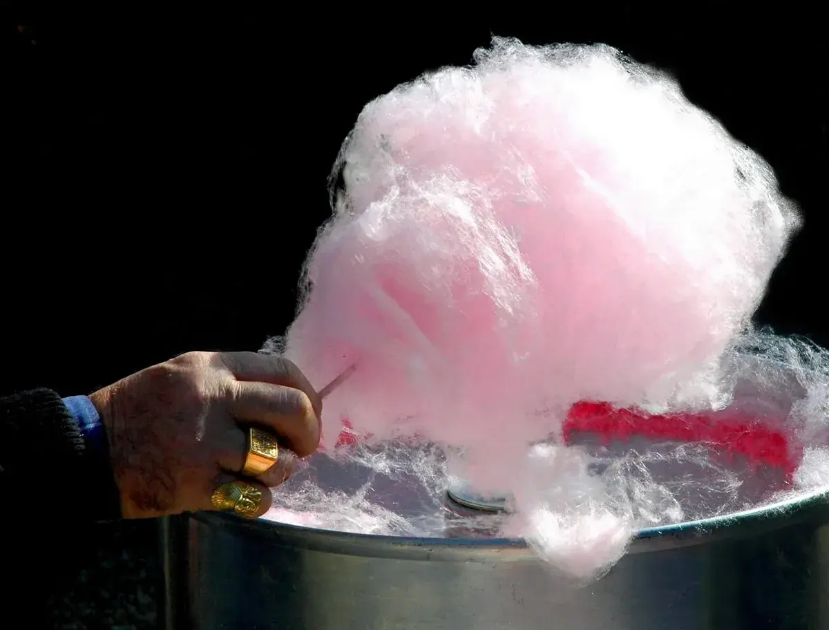 Main d'un homme fabriquant du sucre à barbe à papa rose et blanc.