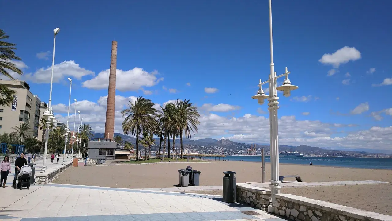 Paseo marítimo con palmeras y chimenea industrial. La playa Misericordia, ideal para llegar y disfrutar del mar.