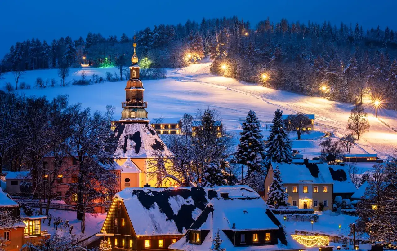 Ein verschneites Dorf in Deutschland, beleuchtet von warmem Licht. Perfekt für einen romantischen Winterurlaub.