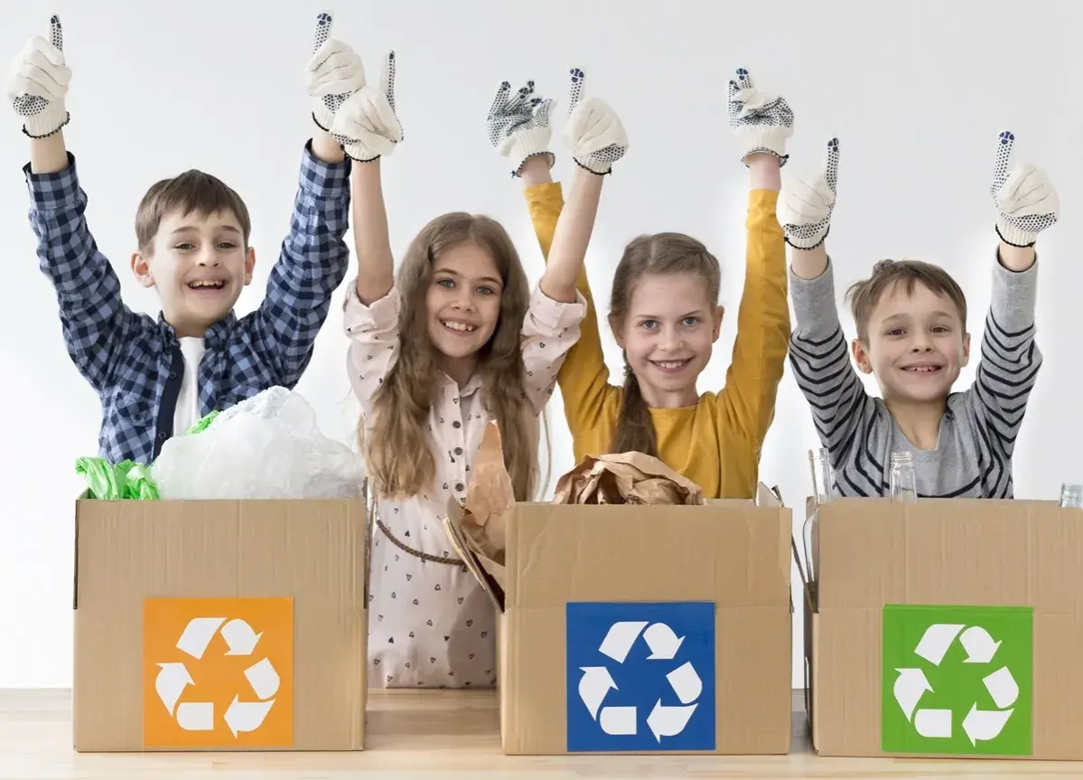 Niños felices participan en un taller de reciclaje, con guantes y pulgares arriba, junto a cajas de cartón con símbolos de reciclaje.