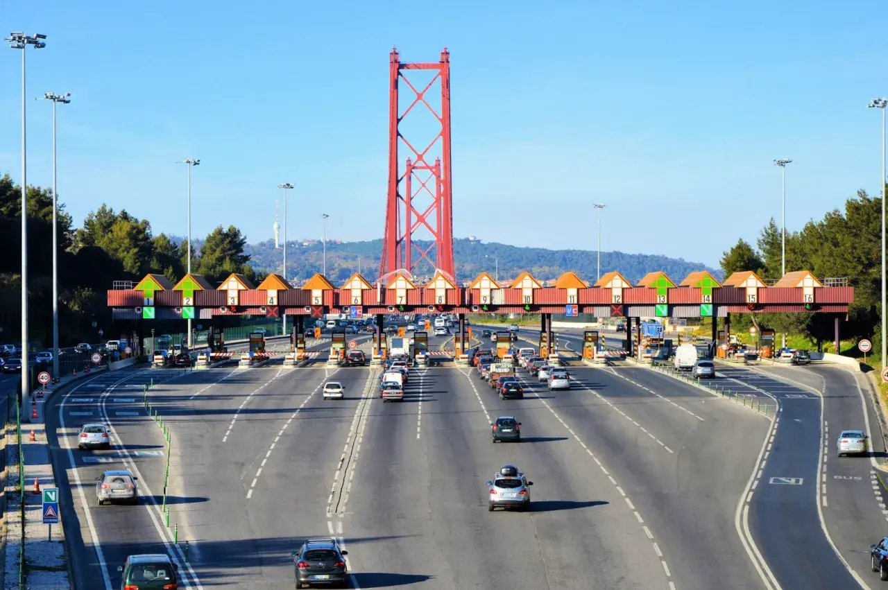 Korkociąg samochodów na autostradach Portugalii, zbliżających się do bramki opłat pod czerwonym mostem.