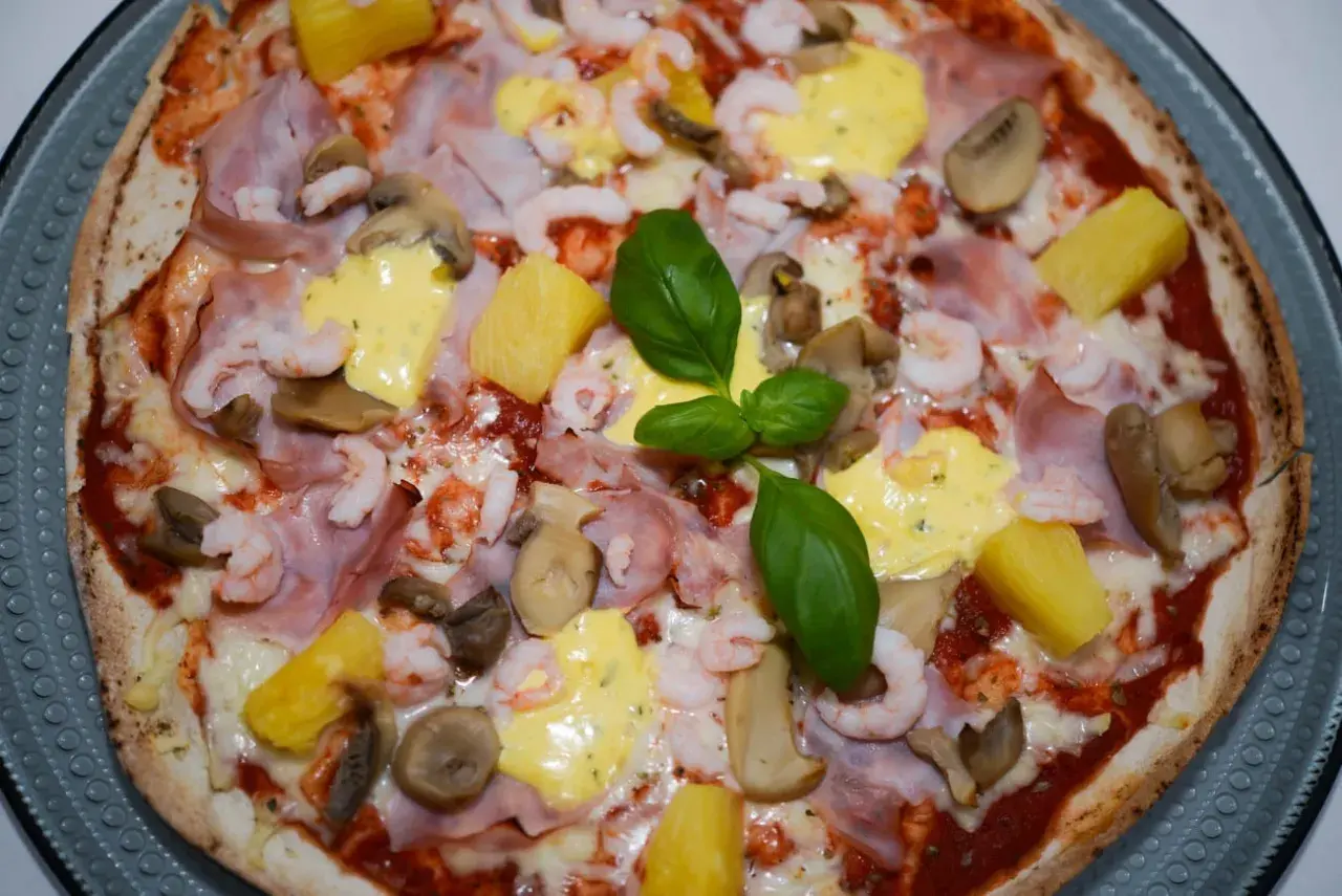 En läcker pizza med räkor och skinka, toppad med ananas, champinjoner och en krämig sås. En riktig smakupplevelse!