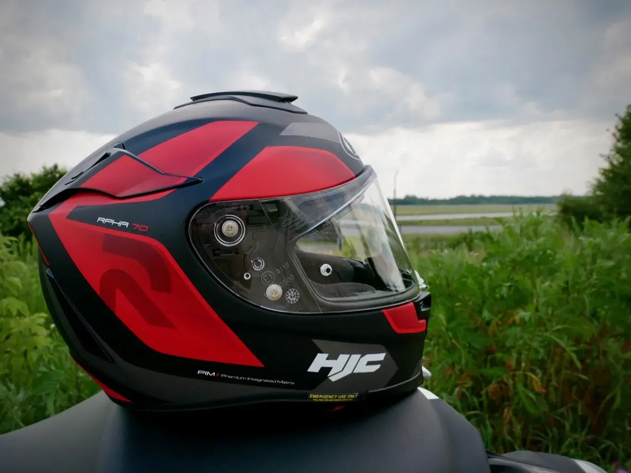 Kask motocyklowy HJC RPHA 70 w czerwono-czarne wzory, gotowy na przygodę na tle zieleni i nieba.