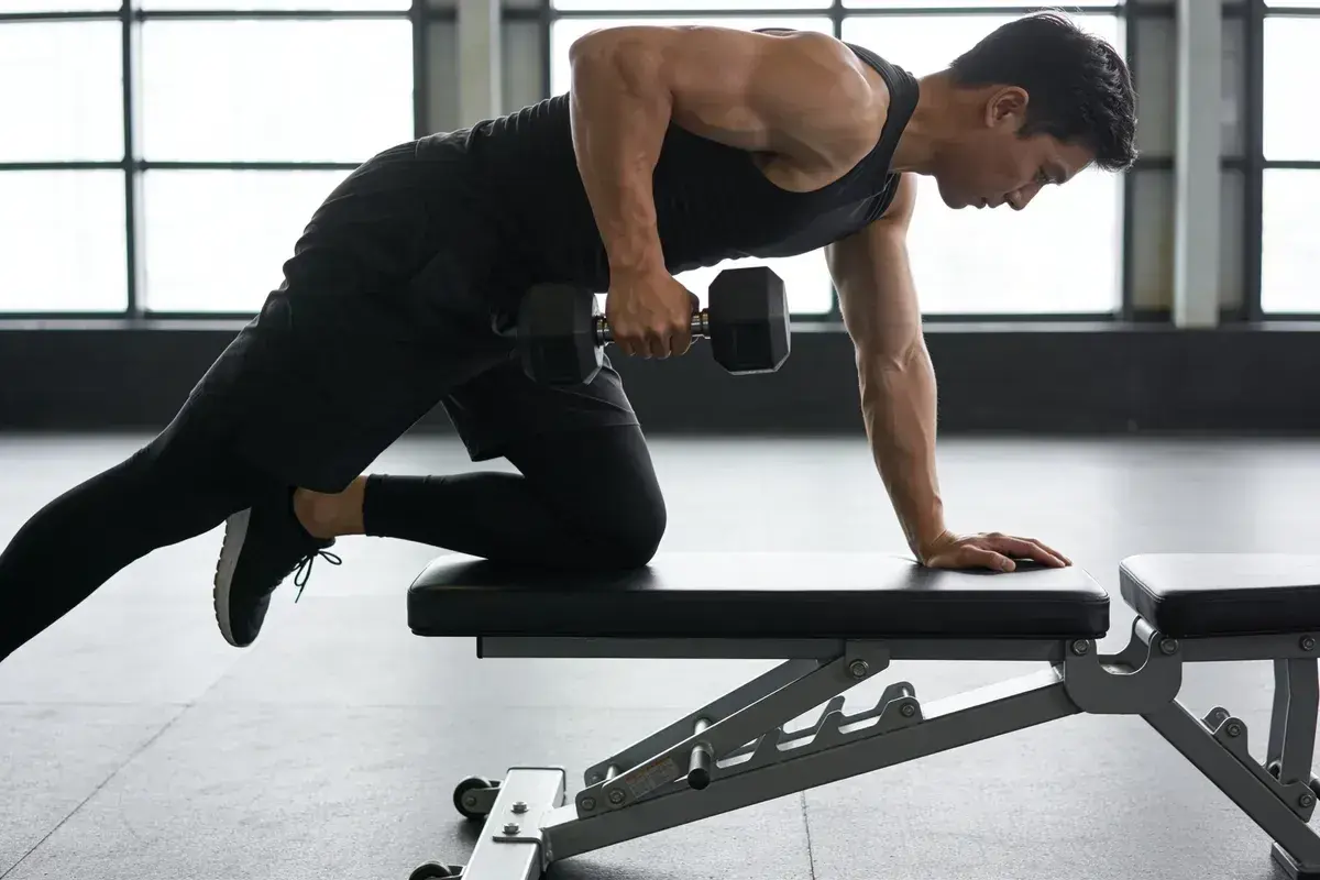 Homme en tenue de sport noir effectuant un rowing haltère sur un banc de musculation, bras tendu, concentré.