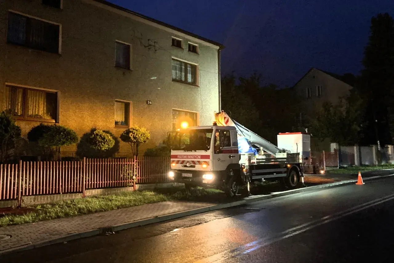 Samochód Tauron z podnośnikiem przy budynku, nocą. Zgłoszenie awarii w toku.
