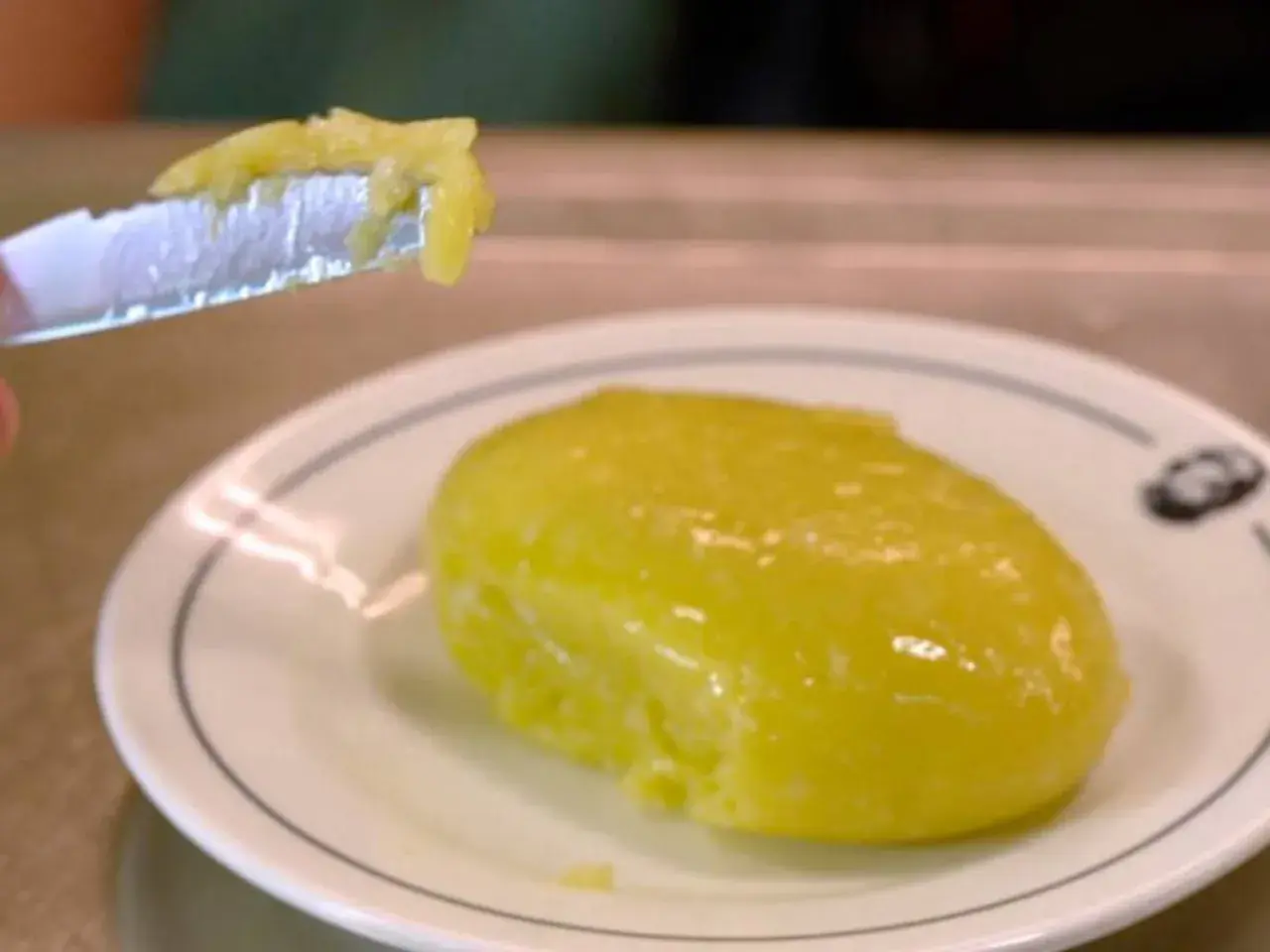 Un trozo de alioli casero untado en un cuchillo, listo para probar la deliciosa salsa sobre un plato blanco.