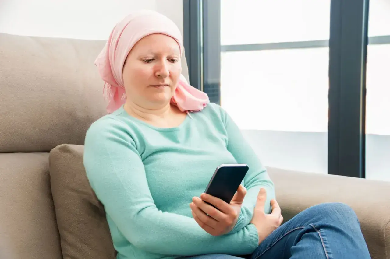 Kobieta w chustce na głowie, po chemioterapii, sprawdza telefon. Może szuka informacji o 500 plus dla chorych na raka ZUS.