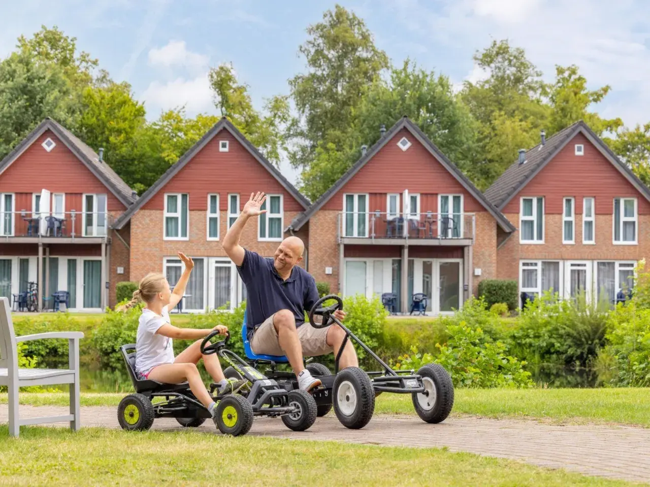 Vater und Tochter winken fröhlich, während sie mit Go-Karts durch die Anlage des TUI Kids Club fahren.