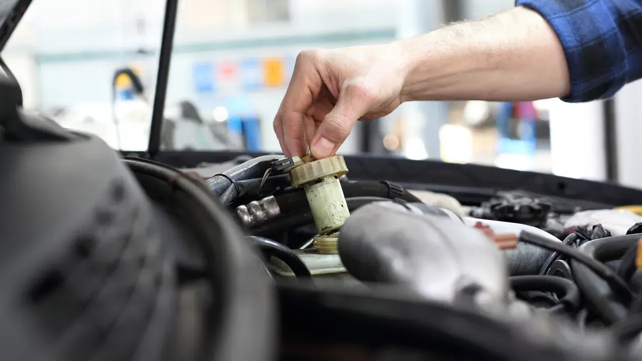 Ręka mechanika odkręca zakrętkę zbiorniczka płynu hamulcowego. Zignorowanie wymiany płynu hamulcowego powyżej 2 lat może prowadzić do awarii.