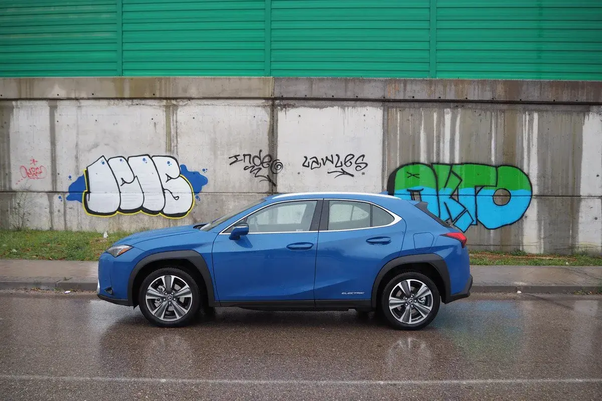 Lexus UX azul aparcado frente a un muro con grafitis. A pesar de los problemas, el coche eléctrico se ve elegante.