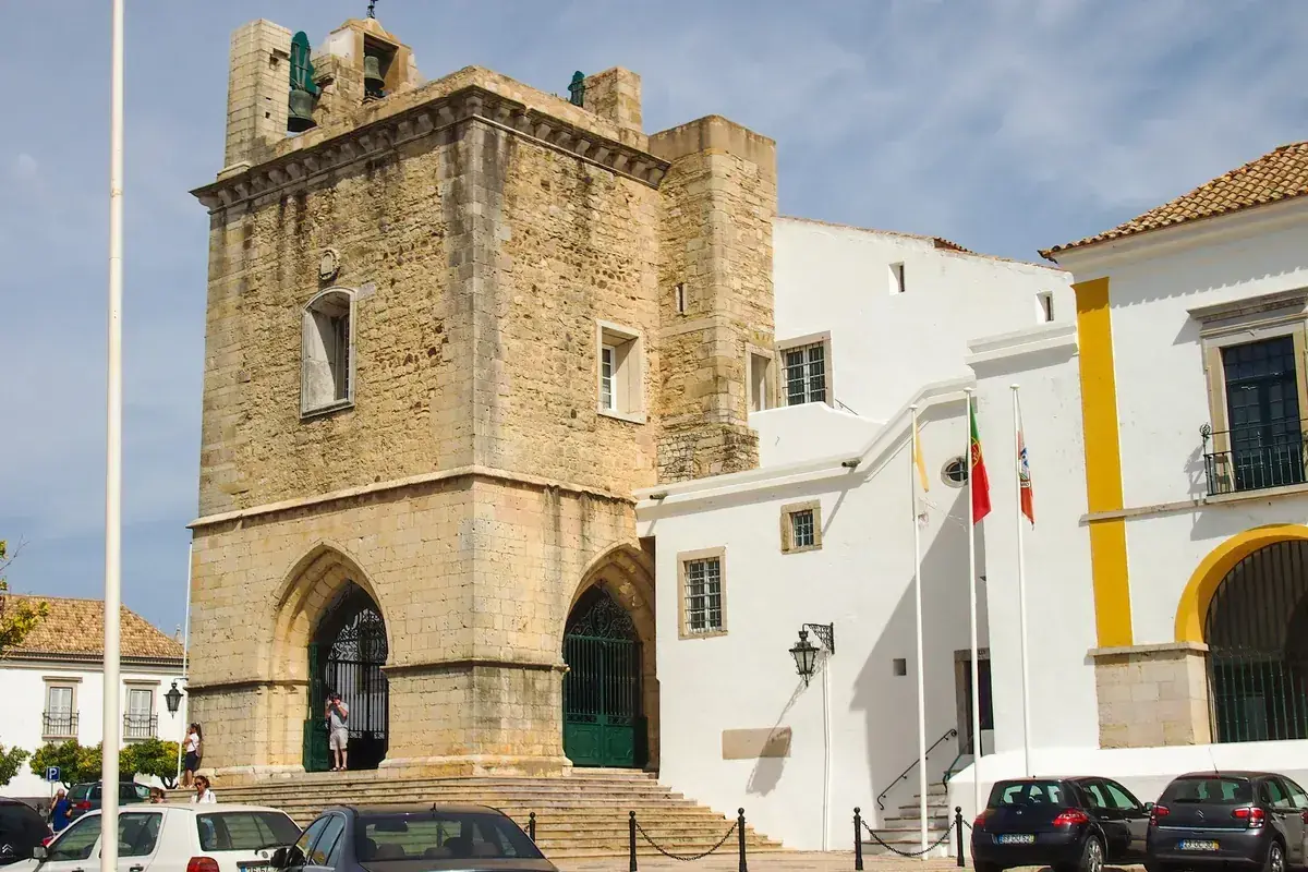 Historisches Gebäude mit Glockenturm in der faro portugal altstadt. Weiße Gebäude mit gelben Akzenten und portugiesische Flaggen.