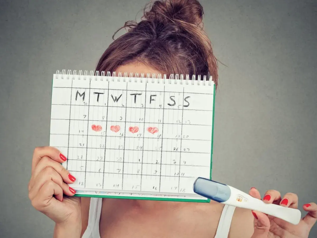 Donna con calendario segnato per il calcolo ovulazione e nidazione, tiene in mano un test di gravidanza.