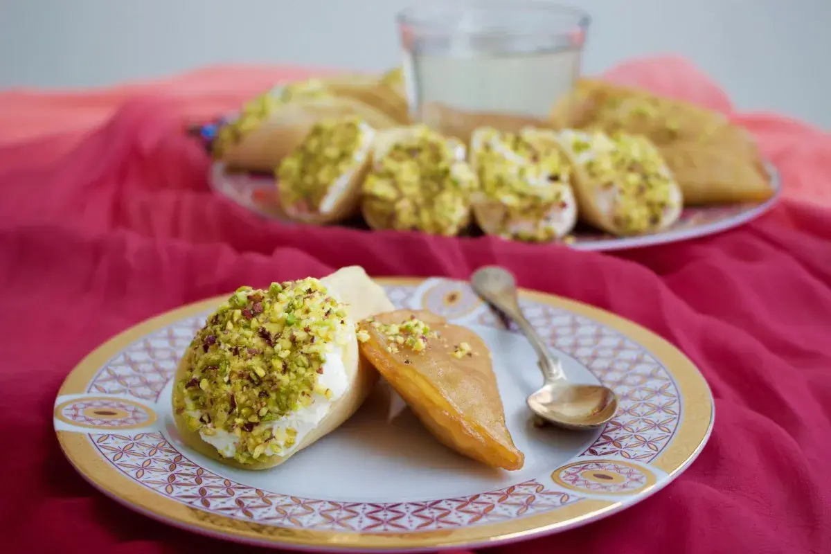Atayef recept: söta pannkakor fyllda med grädde och pistagenötter, serverade på en tallrik med en sked.