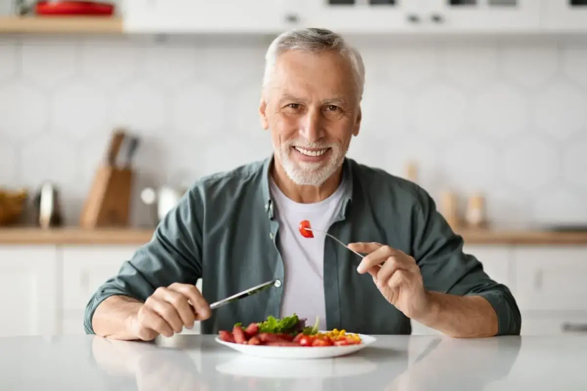 Uomo sorridente mangia cibo sano, godendosi ogni boccone con il suo impianto dentale.