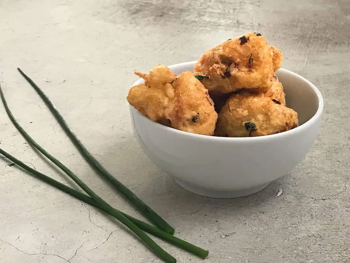 Tazón blanco con buñuelos de bacalao dorados y crujientes, decorado con cebollino fresco.