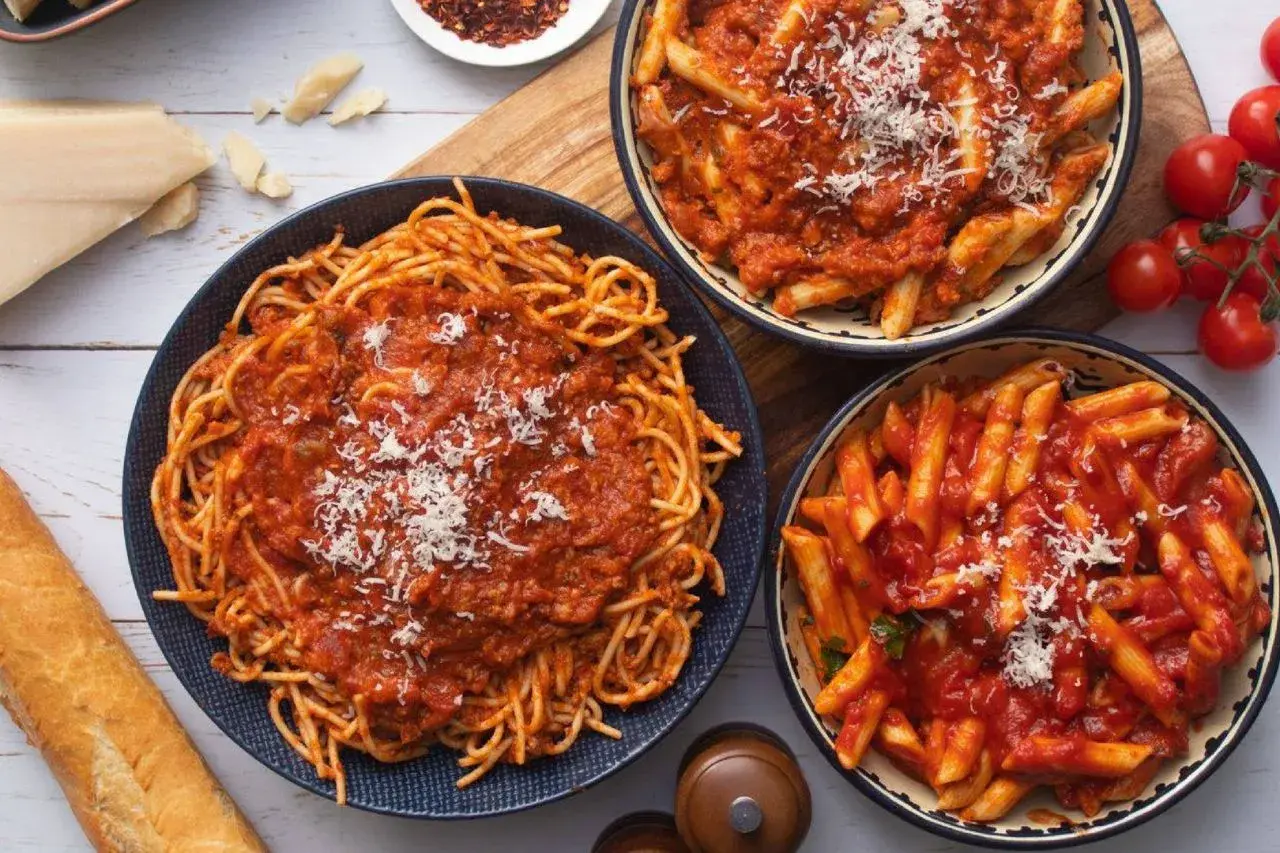 Szybki obiad bez mięsa: spaghetti i penne w sosie pomidorowym, posypane parmezanem. Obok bagietka i pomidorki.