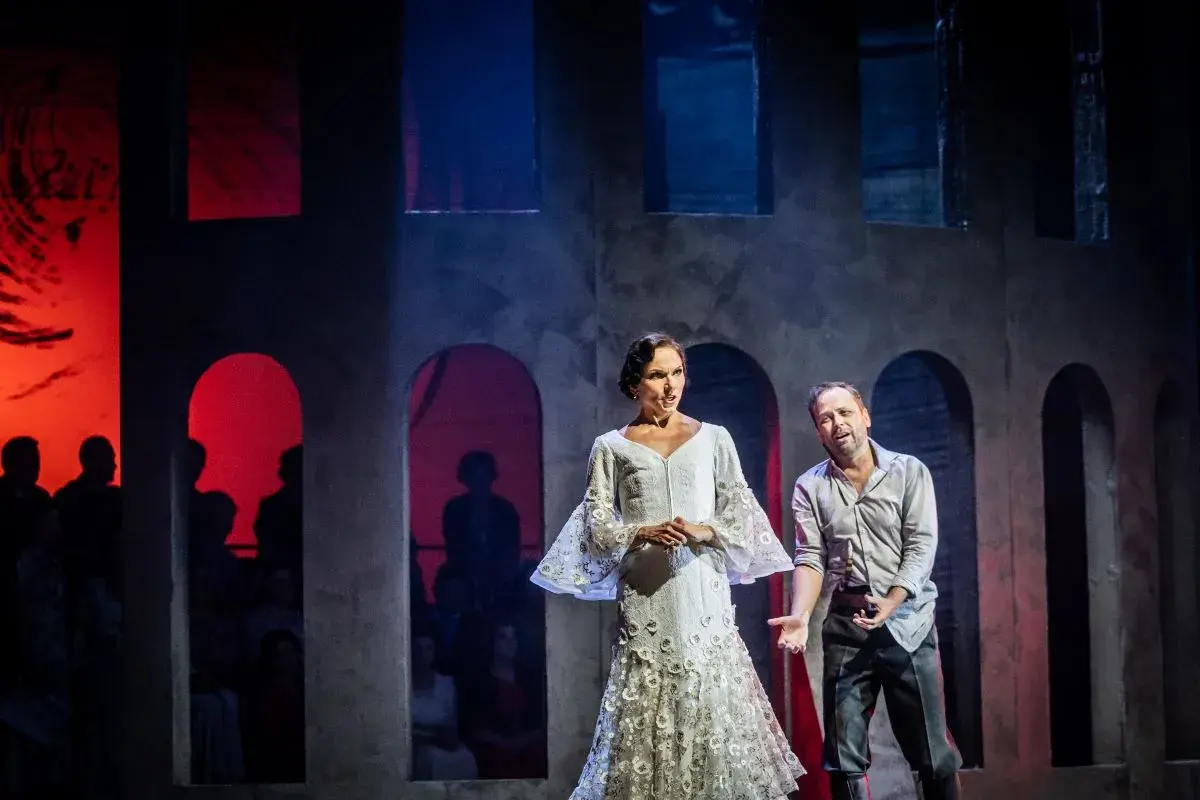Carmen w białej sukni i mężczyzna na scenie operowej. Tło z łukami i czerwonymi światłami.
