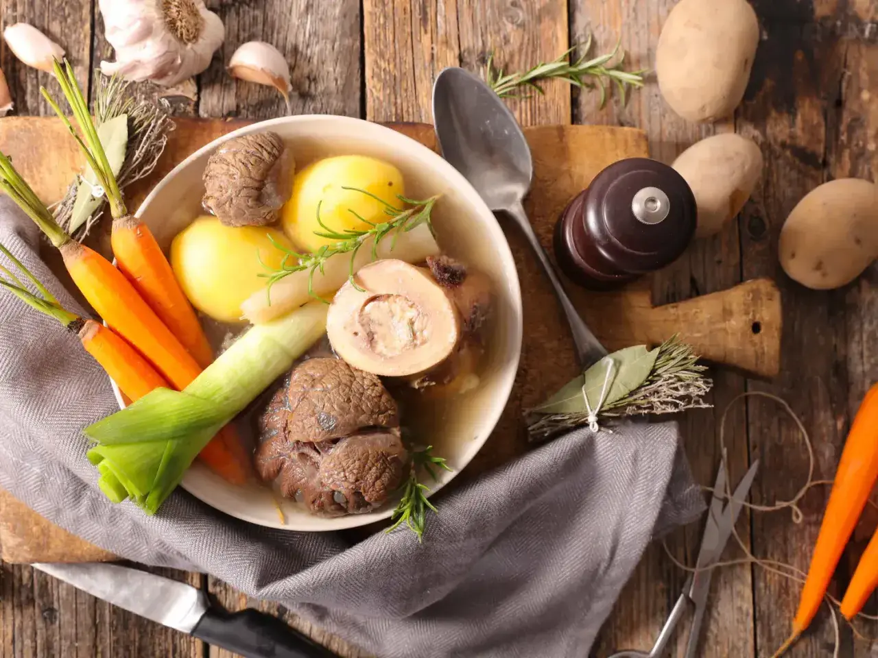 Un bol de pot-au-feu fumant avec des carottes, des pommes de terre, du poireau et de la viande. Des herbes et de l'ail complètent ce plat réconfortant.