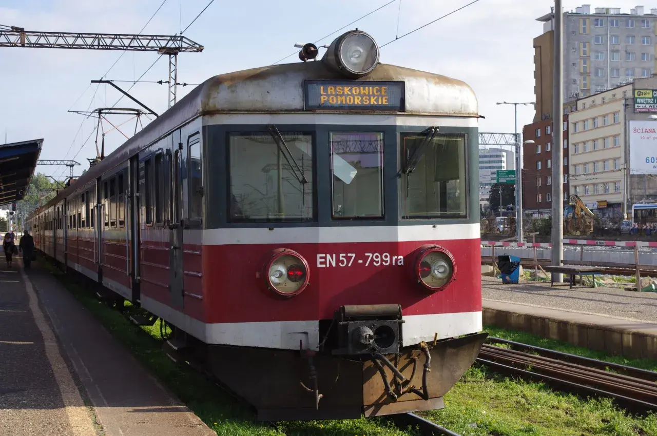 Pociąg EN57-799ra z napisem LASKOWICE POMORSKIE na tablicy. Stoi na peronie, w tle budynki i trakcje kolejowe.