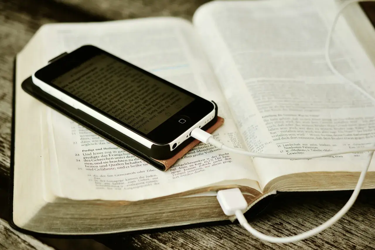 Nowoczesna biblia na co dzień: smartfon z tekstem biblijnym leży na otwartej księdze, podłączony do ładowania.