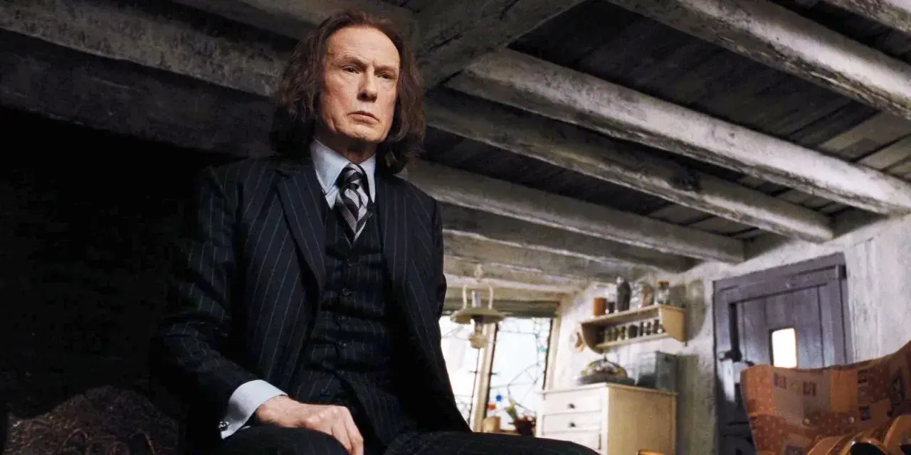 Bill Nighy jako Rufus Scrimgeour w Harry Potterze, w garniturze, siedzi w ponurym wnętrzu.